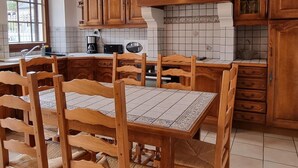 Keittiössä on puiset kaapit, laatoitettu seinäosa työtason yläpuolella, ruokapöytä tuoleineen ja ikkuna, josta on näkymä.