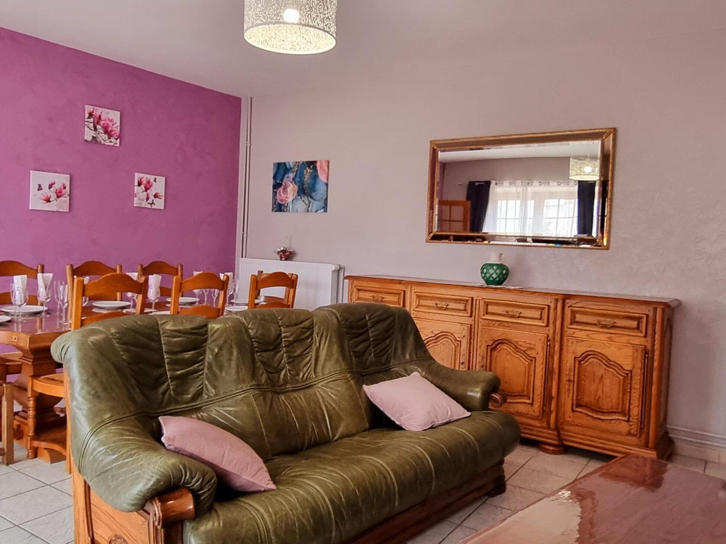 Un salon avec un canapé en cuir vert, une table à manger en bois, des chaises, un buffet et des œuvres d’art murales.