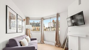 Ein modernes Wohnzimmer mit einer Couch, einem Flachbildfernseher und Blick auf die Stadt.