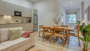Un saló modern amb un sofà, una taula de menjador amb cadires, una zona de cuina amb nevera i un finestral gran.