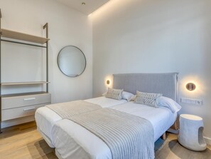 Ein Schlafzimmer mit Bett, Nachttischen, einem Kleiderschrank, einem runden Spiegel und Wandleuchten.