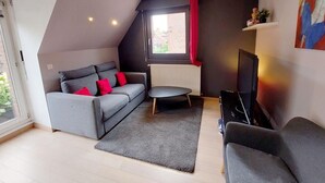 Un salon moderne avec un canapé gris, une petite table ronde, un téléviseur et un radiateur.