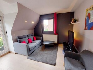 Un salon moderne avec un canapé gris, une petite table ronde, un téléviseur et un radiateur.