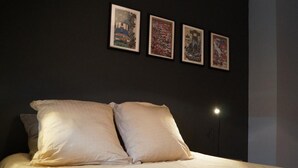 Un lit avec deux oreillers, un mur sombre et trois tableaux encadrés.