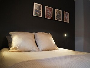 Un lit avec deux oreillers, un mur sombre et trois tableaux encadrés.