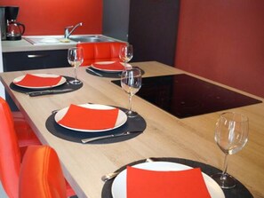 Une table à manger est dressée avec des serviettes rouges, des assiettes et des verres à vin, et on peut apercevoir une chaise rouge.