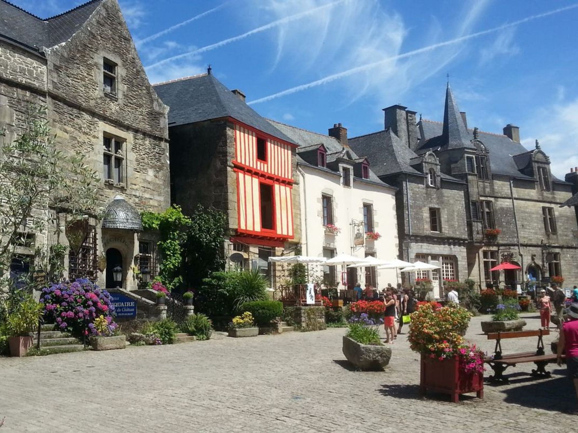 A historic stone building with a red facade, a cobblestone courtyard, and outdoor seating areas.