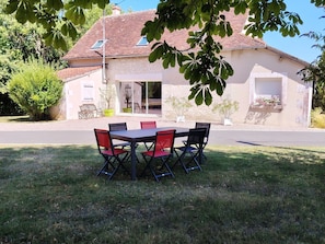 Une maison avec un toit en tuiles, une terrasse avec une table et des chaises, et un jardin avec un arbre.