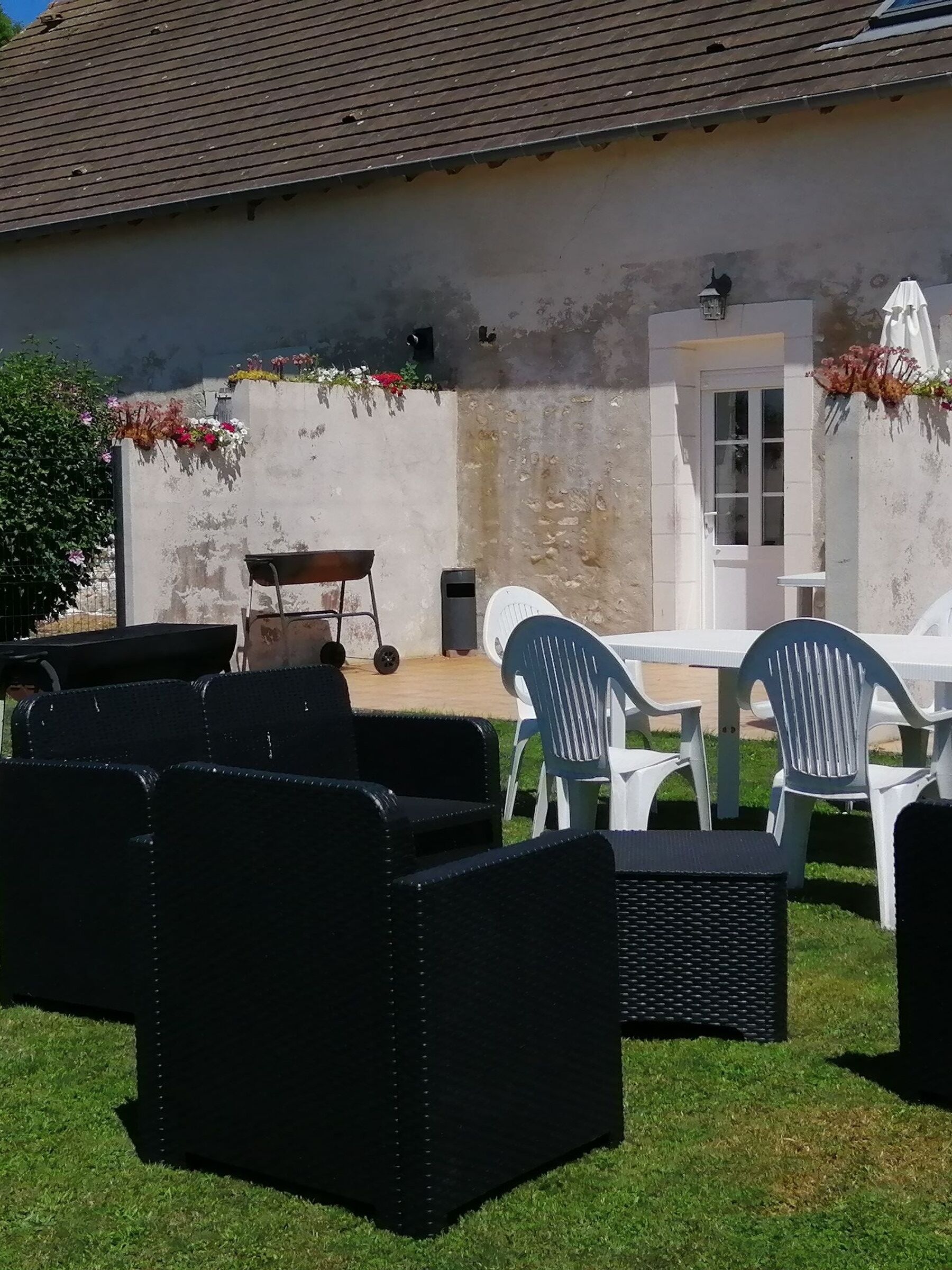Un patio al aire libre con mesa y sillas, un carretilla y un muro de hormigón con jardineras.