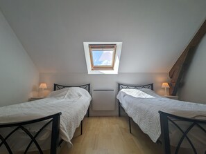 Une petite chambre bien éclairée, avec deux lits simples, une lucarne et des lampes de chevet.