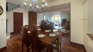A dining area with a chandelier, wooden dining table, chairs, and a view to a living room. - Spacious house with garage - 6 guests (Banyuls-sur-Mer)