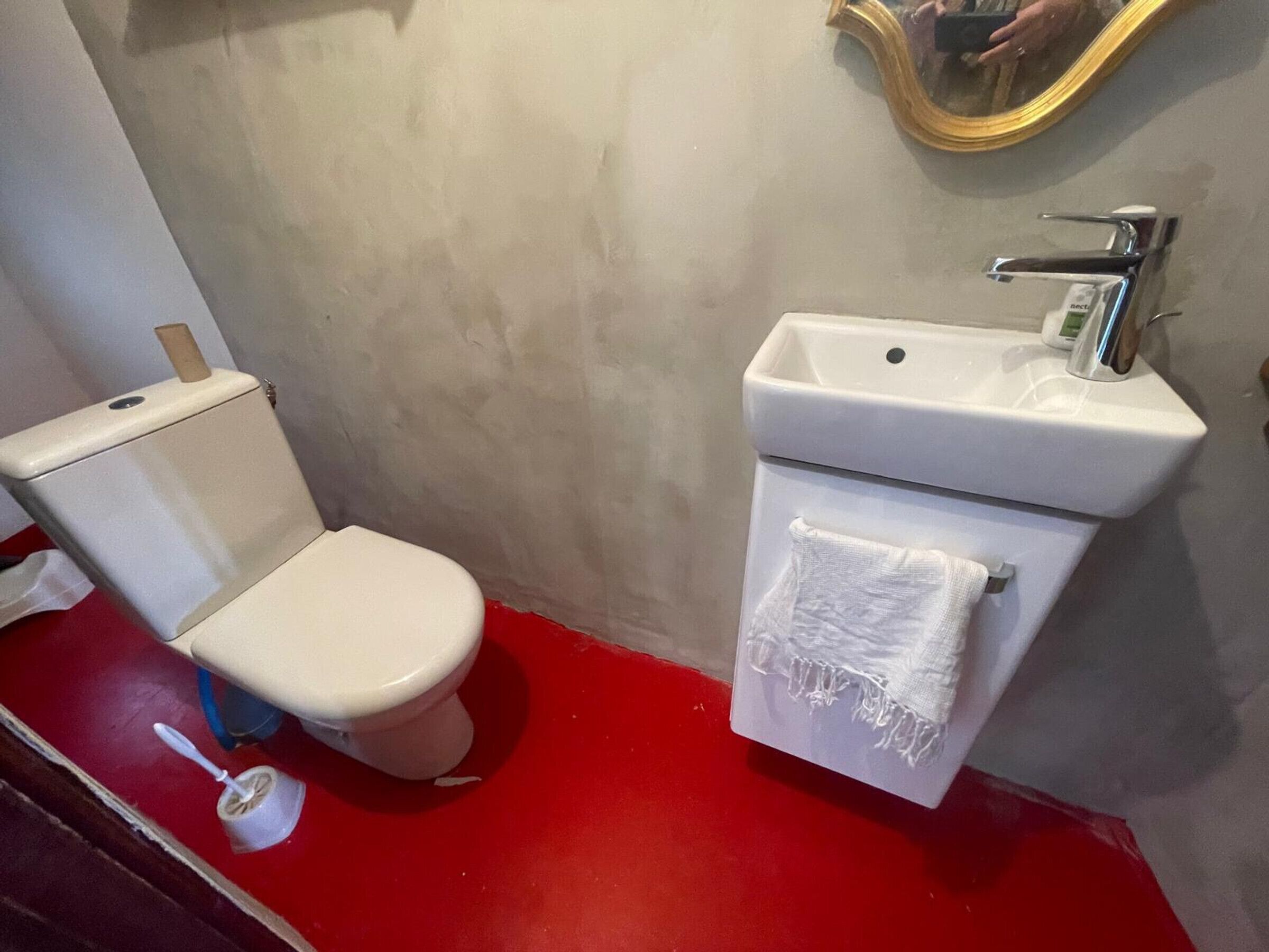 A bathroom with a white toilet, a sink with a towel, and a mirror on the wall.