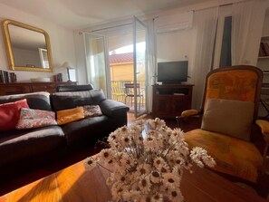 A living room with a sofa, armchair, TV, and a vase of flowers. - Spacious house with garage - 6 guests (Banyuls-sur-Mer)