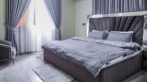 A modern bedroom with a large bed, grey curtains, an air conditioning unit, and a grey sofa.
