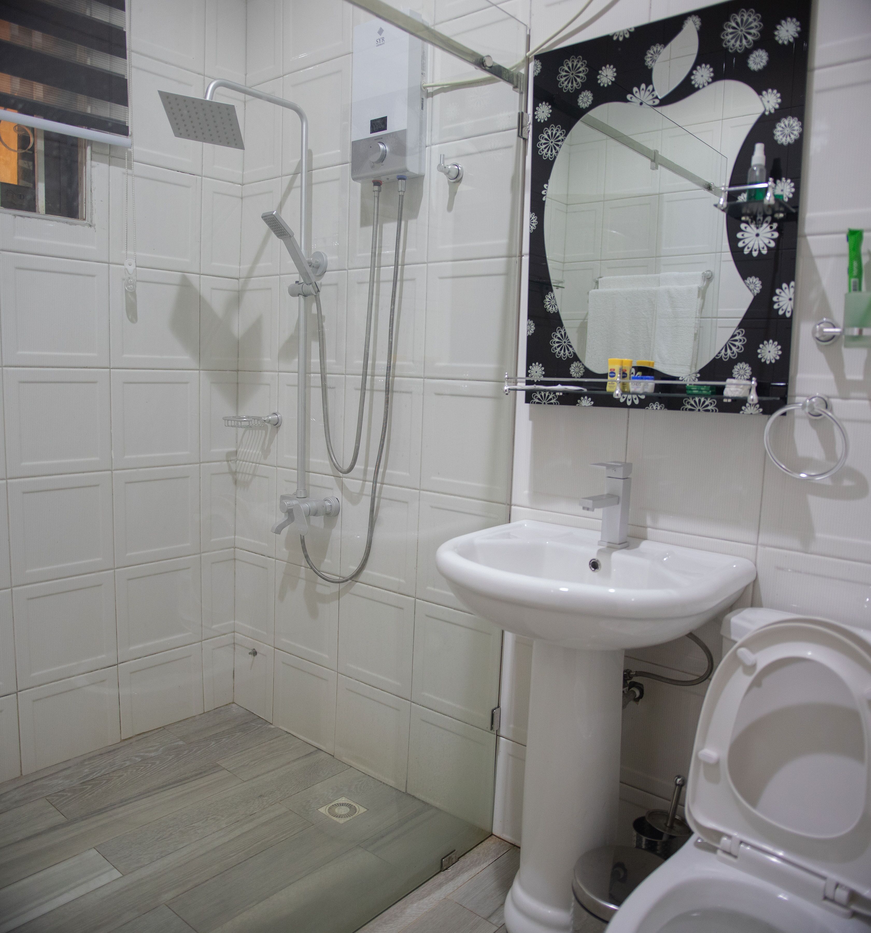A bathroom with a shower, sink, toilet, and a mirror with a floral design.