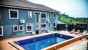 A swimming pool with a blue tiled deck, a building with multiple windows and air conditioning units, and a stone pathway.