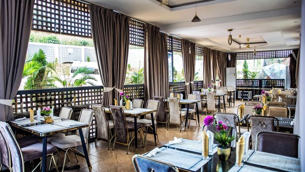 A restaurant with multiple tables and chairs, ceiling fans, and large windows with curtains.