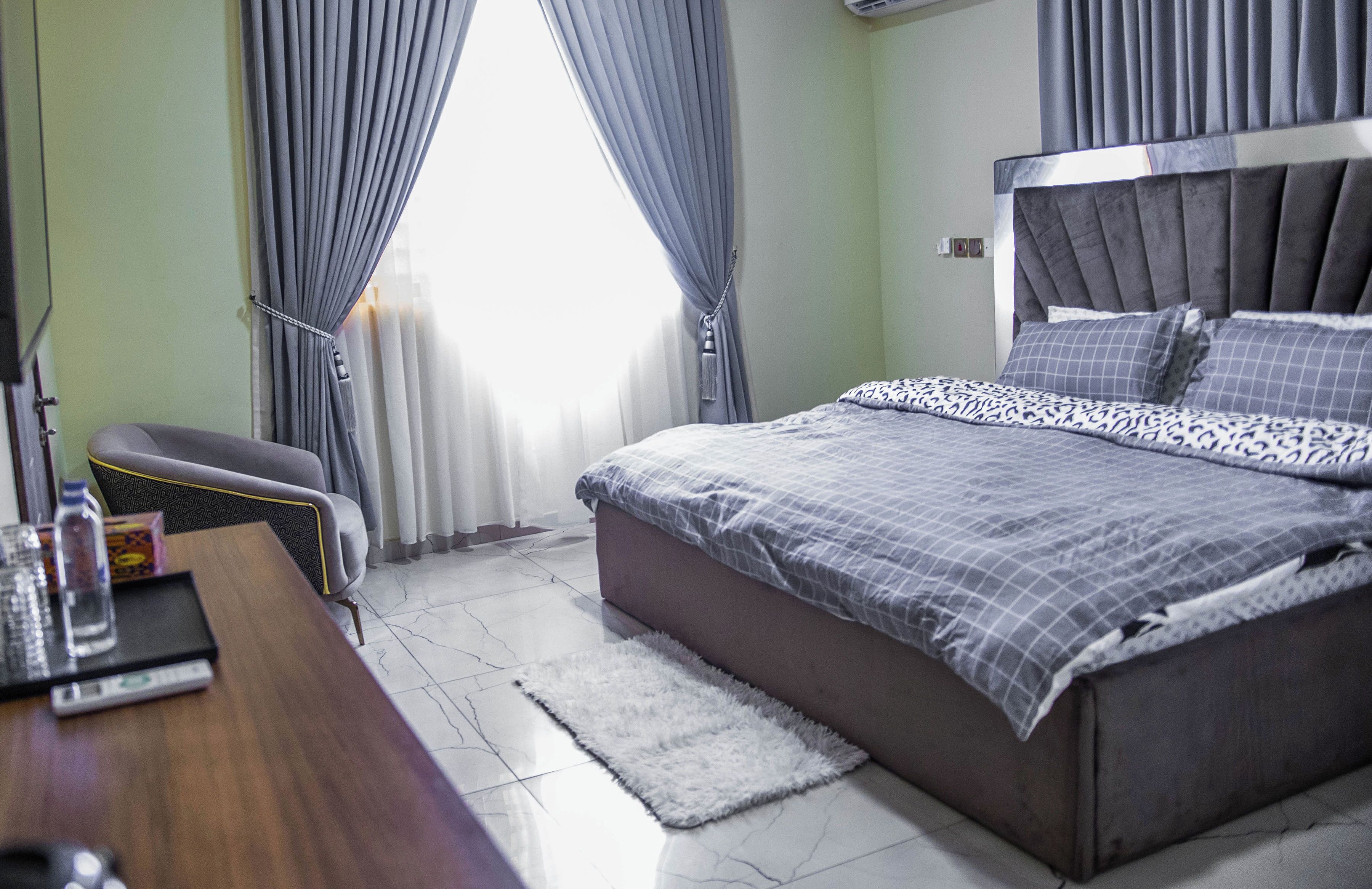 A bedroom with a bed, a desk, a chair, and curtains.