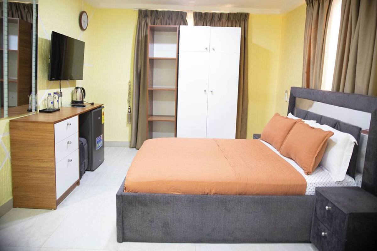 A bedroom with a bed, a TV, a wardrobe, and a desk with a kettle.