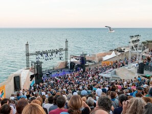 Ein belebtes Open-Air-Event mit Bühne und Publikum am Meer.