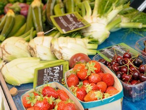 Eine Auswahl an frischen Früchten und Gemüsen, darunter Erdbeeren, Kirschen und Artischocken, präsentiert in einer Marktlage.