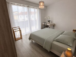 Ein Schlafzimmer mit Bett, Schreibtisch, Stuhl, einem Topf mit Pflanze und einer Pendelleuchte.