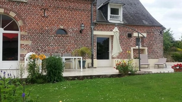 Une maison en briques dotée d’un patio couvert, d’une pelouse et de meubles de jardin.