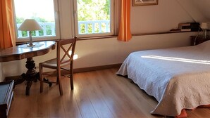 Une pièce comprenant un lit, une chaise, une table avec une lampe et une fenêtre avec des rideaux.