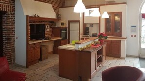 Une cuisine avec un mur en briques, des armoires en bois, un îlot central, des luminaires suspendus et une chaise rouge.