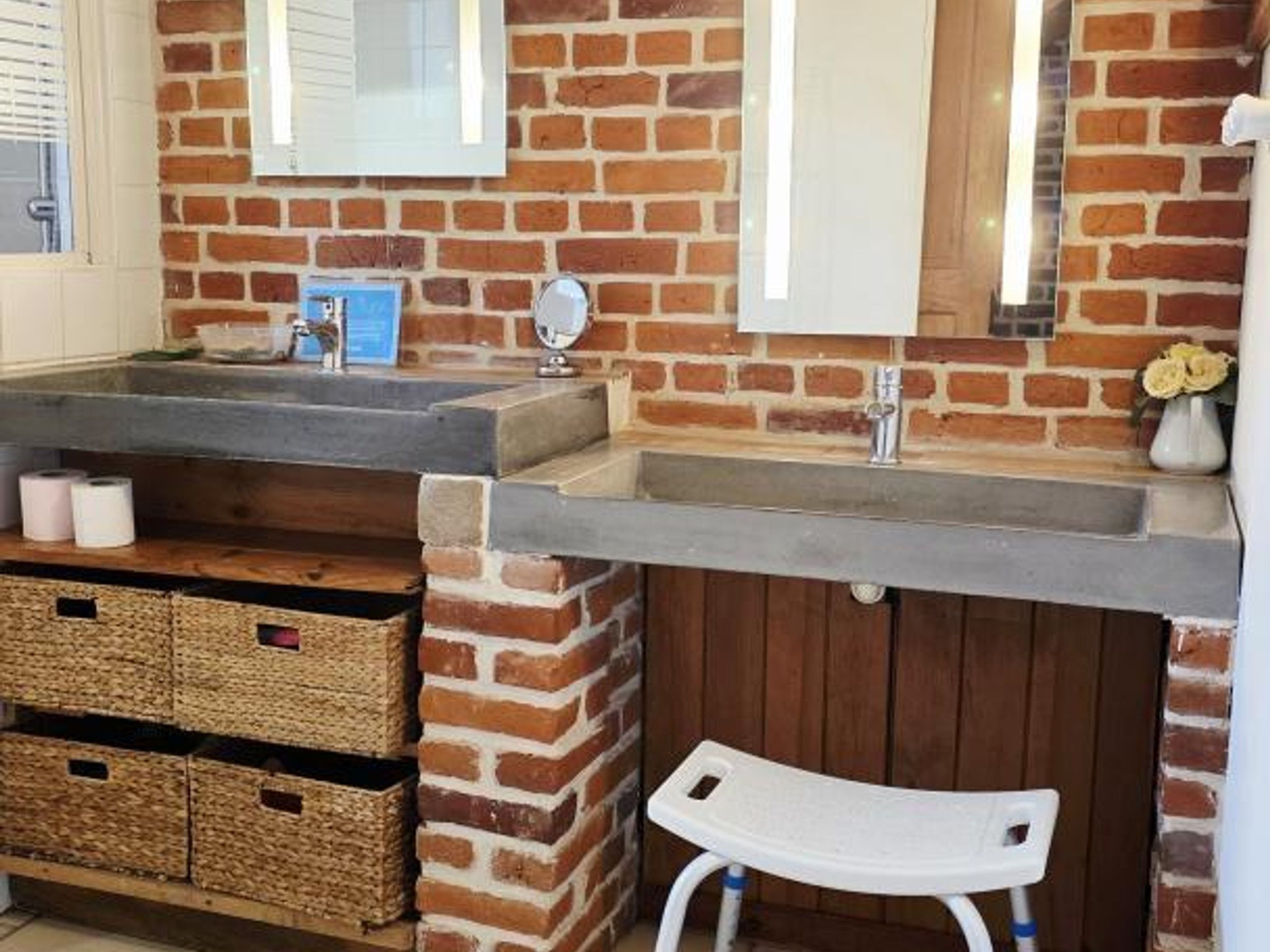Une salle de bain avec un mur en briques, un lavabo avec un miroir et un petit tabouret.