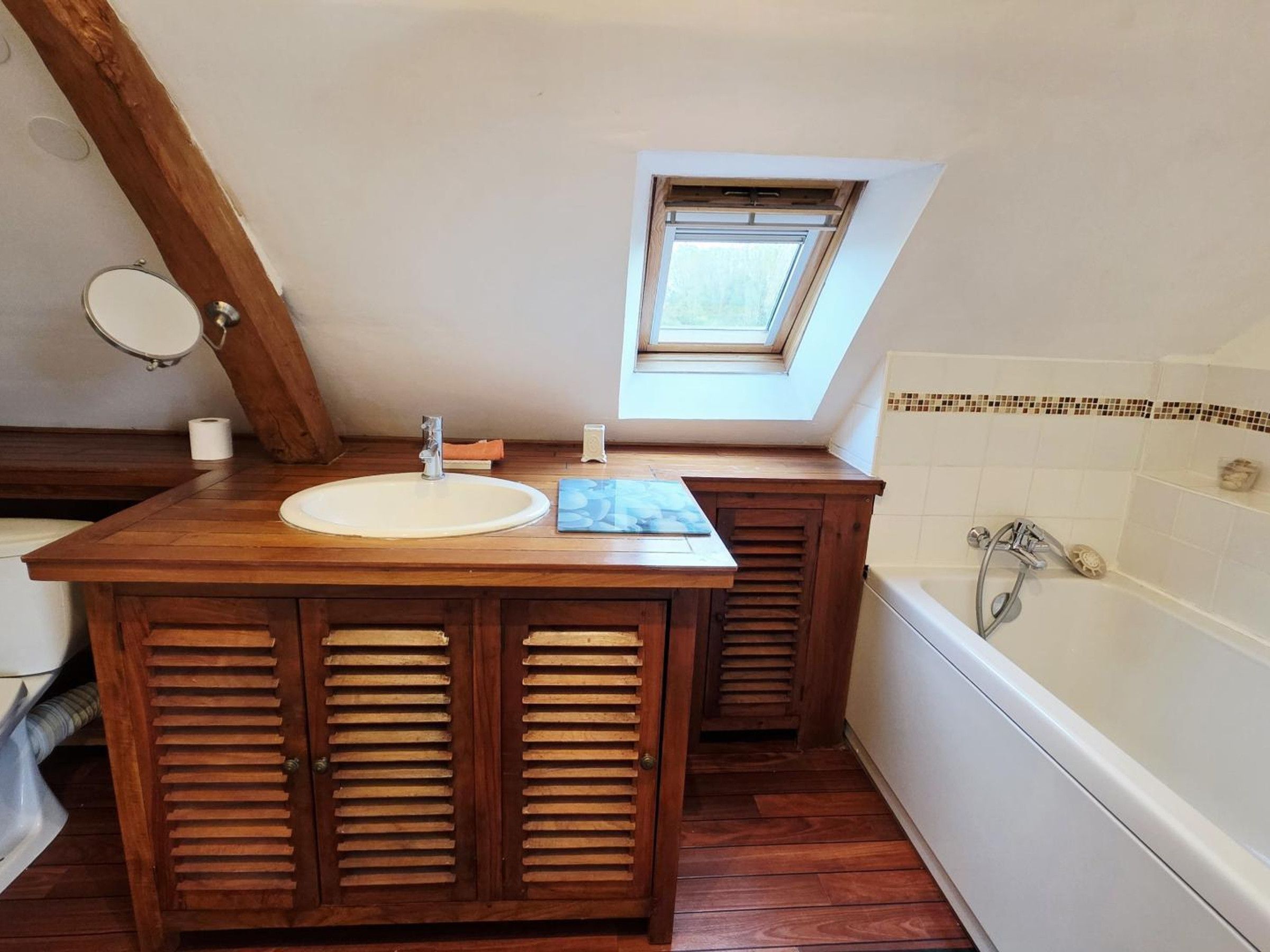 Een badkamer met een houten wastafelmeubel, een wastafel, een raam en een bad.