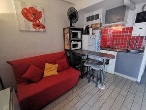 Eine kleine Küche mit einem roten Sofa, einem Ventilator, einer Mikrowelle, einem Kühlschrank und einem Waschbecken.