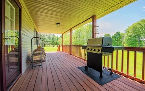 Una terraza techada con una parrilla, escalones de madera y vista a un jardín con césped.