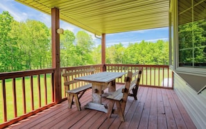 Una terraza de madera con una mesa y bancos, rodeada por una barandilla, con vistas a un paisaje verde.