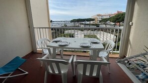 En balkong med ett bord dukat för två personer, vita stolar och en blå hopfällbar stol.