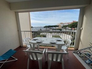 A balcony with a table set for two, white chairs, and a blue folding chair. - Apartment with parking - 6 guests (Cap d'Agde)