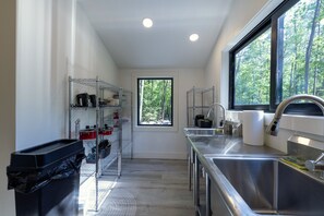 A modern kitchen with stainless steel appliances, a window with a forest view, and a trash bin.