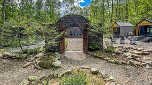 Een stenen bogenpoort die leidt naar een gebouw, omringd door bomen en een grindpad.