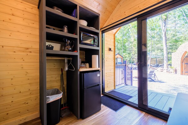 A compact kitchen with a built-in refrigerator, shelves with various items, and a sliding glass door leading to an outdoor deck.
