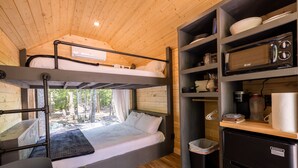 Een slaapkamer met stapelbedden, een kitchenette, een koelkast en een raam met uitzicht op een bos.