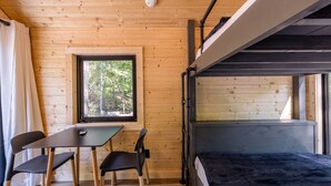 Interieur van een houten hutje met een stapelbed, een tafel met stoelen, een raam met uitzicht op bomen en een plafondlamp.