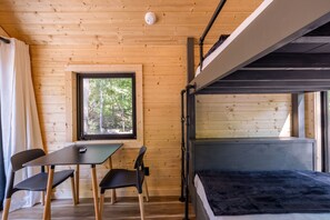 L’intérieur d’un chalet en bois comprend un lit superposé, une table avec des chaises, une fenêtre donnant sur les arbres et un luminaire fixé au plafond.