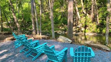 A row of turquoise Adirondack chairs facing a forested area with a stream.