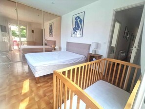 Ein Hotelzimmer mit zwei Betten, einem Holckrippe, einem Spiegel und einer Tür, die auf einen Balkon führt.