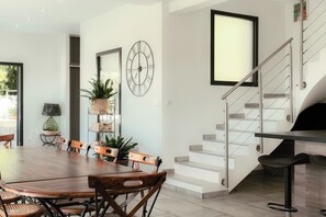 Ein Essbereich mit einem Holztisch und Stühlen, eine Treppe mit Glastrennwand und eine an der Wand befestigte Uhr.
