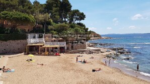 Ein Strand mit einem Steinhaus, einem Restaurant und Blick aufs Meer.