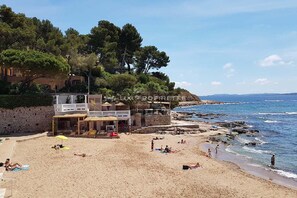 Ein Strand mit einem Steinhaus, einem Restaurant und Blick aufs Meer.