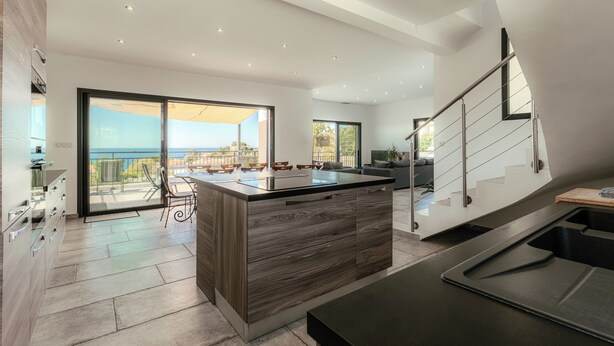 Una cocina amplia con una isla grande, un comedor con asientos exteriores y vistas al mar.