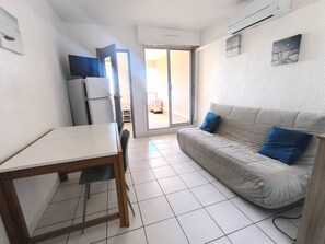 Ein kompakter Wohnraum mit Esstisch, einer Couch, einem Kühlschrank und einer Glastür zum Außenbereich.