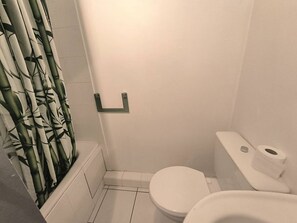 Ein Badezimmer mit Toilette, einer Duschvorhang mit Bambusmuster und einem Toilettenpapierhalter.